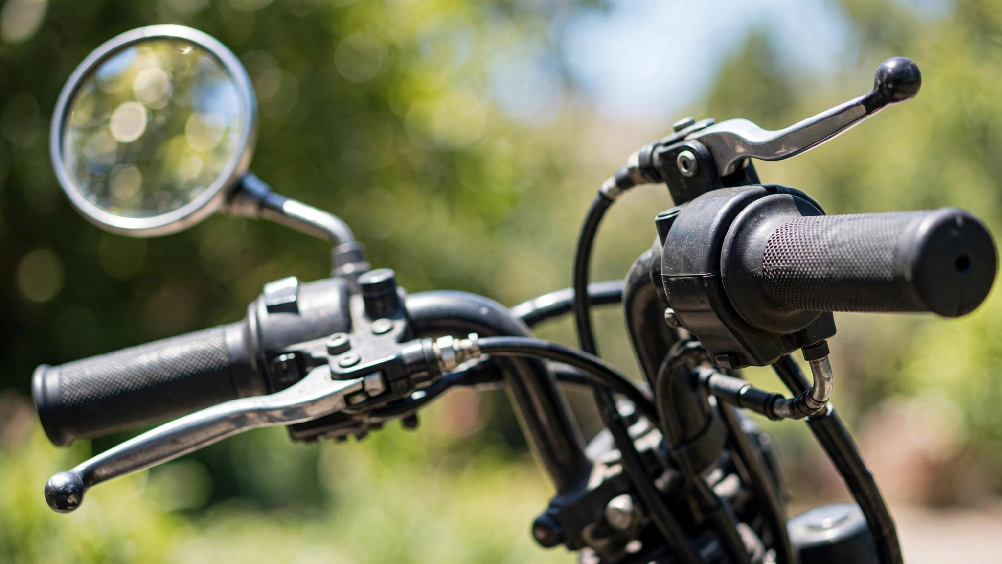 Close-up of motorcycle handlebar controls including the throttle grip, clutch lever, front brake lever and rear-view mirror