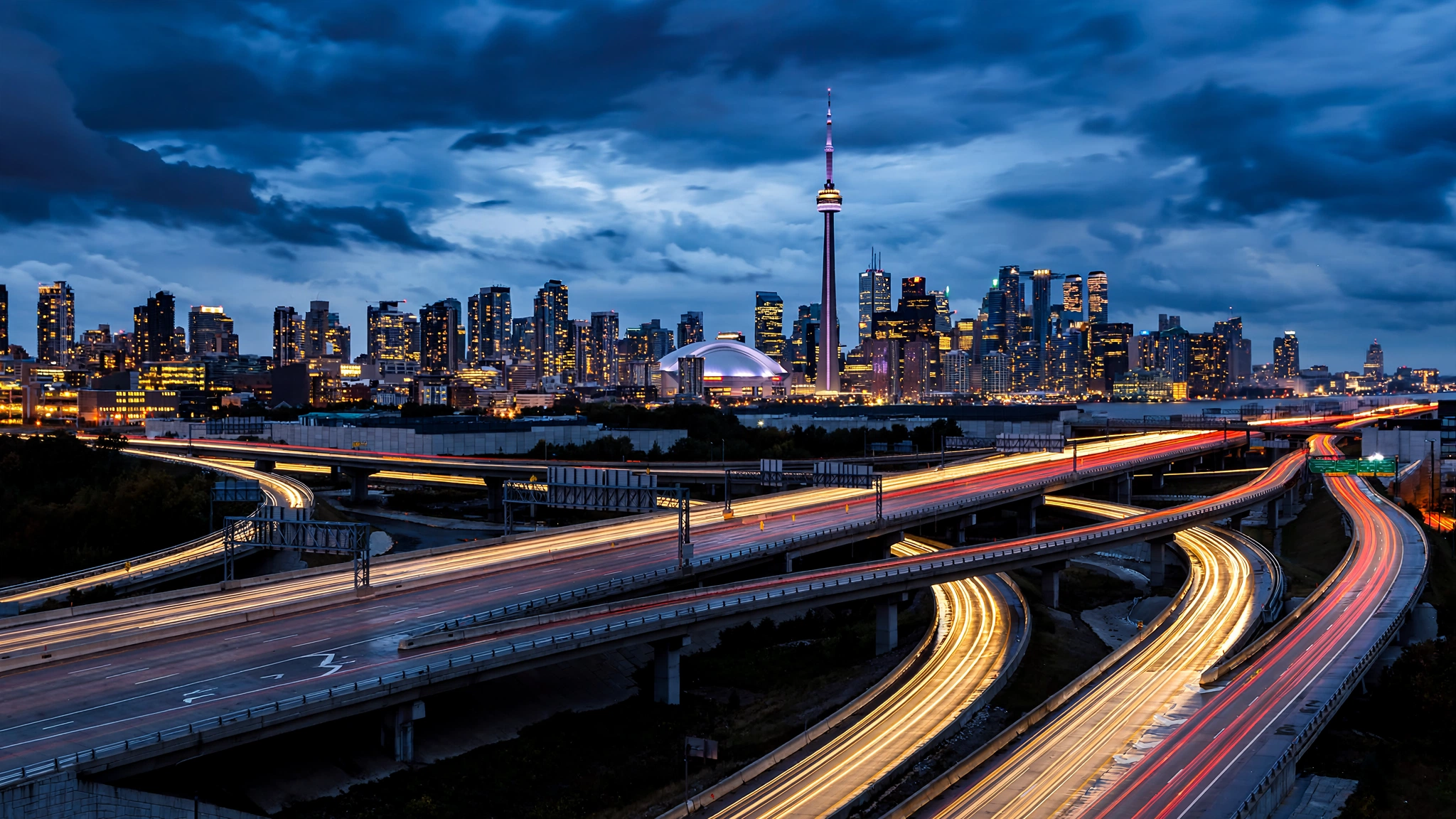 Toronto skyline with the CN Tower at blue hour viewed from a multi-lane Ontario highway interchange with light trails
